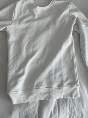 Vit sweatshirt från Moncler - Säljer en stilren vit sweatshirt från Moncler med rund halsringning och ribbade muddar. Tröjan har en diskret Moncler-logga på ena ärmen och är tillverkad i mjukt bomullsmaterial. Perfekt för en clean och avslappnad look.