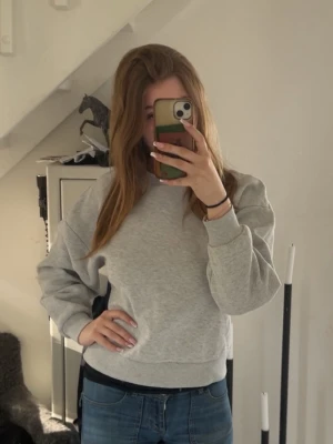 Ljusgrå basic sweatshirt - En stilren ljusgrå sweatshirt med rund hals och ribbade muddar. Tröjan har en avslappnad passform och är tillverkad i mjukt material, perfekt för en casual look. Passar till jeans eller leggings för en enkel och snygg outfit.