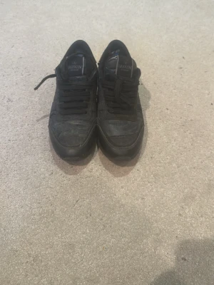 Svarta sneakers från Valentino storlek 38 går att lägga in på lagning - Snygga svarta sneakers från Valentino Garavani med klassisk låg profil och svarta skosnören. Skorna har en diskret logga på plösen och är tillverkade i en mix av textil och läder. Perfekta för dig som gillar stilrena och exklusiva sneakers.
