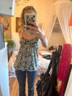Mönstrad linnetopp med smala axelband - Snygg linnetopp med svart och vit blommig design. Toppen har smala axelband och en lätt utställd passform med v-ringning. Perfekt för dig som gillar en feminin och avslappnad stil. Materialet känns mjukt och svalt mot huden.