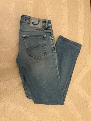Jacob Cohën blåa jeans - Snygga blåa jeans från Jacob Cohën med klassisk femficksdesign. Det är storlek 34 som passar W30-31 L32 Jeansen har en patch med J-logga bak i midjan och är tillverkade i mjuk denim med lätt tvättad look. Perfekta för en avslappnad stil. Jacob coven märket är speciellt med häst hår vilket är rätt sällsynt nu för tiden 🐎 fina unika knappar. 