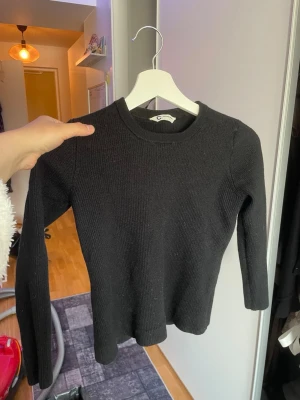 Svart ribbstickad tröja - En stilren svart tunn stickad tröja med rund hals och långa ärmar. Tröjan har en ribbstickad struktur. Perfekt för en avslappnad stil.