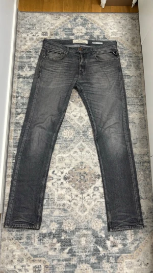 Replay Jeans Grover  - Säljer ett par grå slim fit jeans från Replay med snygga fades detaljer och klassiska fem fickor. Jeansen har en modern passform och är tillverkade i bomull. Perfekt för dig som gillar en stilren och trendig look.