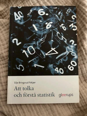 Att tolka och förstå statistik - Boken 'Att tolka och förstå statistik' av Silje Bringsrud Fekjær är en kursbok inom statistik. Omslaget är svartvitt med tärningar och siffror, och boken har mjuka pärmar. Perfekt för dig som pluggar statistik eller samhällsvetenskap.
