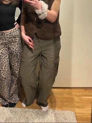 Olivgröna cargobyxor med fickor - Säljer ett par olivgröna cargobyxor med raka, vida ben och klassiska sidofickor med lock. Byxorna har normal midja och är tillverkade i ett slitstarkt bomullstyg. Perfekta för en avslappnad och trendig streetstil. Jag är 178cm och byxorna har blivit lite korta för mig men annars supersköna byxor✨