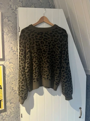 Leopardmönstrad stickad tröja JDY - Cool stickad tröja från JDY i storlek XL (väldigt liten i storlek, passar bra på S/M)  med leopardmönster i svart och mörkgrönt. Tröjan har rund halsringning, ribbade muddar och avslappnad passform. Perfekt för dig som vill ha en trendig och bekväm look. Har en liten tråd som hänger ut vid armen, syns inte. 💘