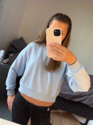 Ljusblå croppad hoodie Gina Tricot - Snygg ljusblå croppad hoodie från Gina Tricot med rund halsringning och breda muddar vid ärmslut och nederkant. Mjuk bomullskänsla och enkel design som passar perfekt till jeans eller leggings.