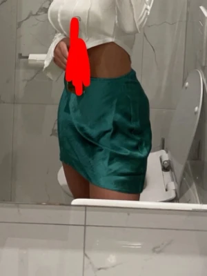 Grön satin kortkjol - Säljer en snygg grön kortkjol i glansigt satinmaterial. Kjolen har en enkel, rak passform och sitter högt i midjan.
