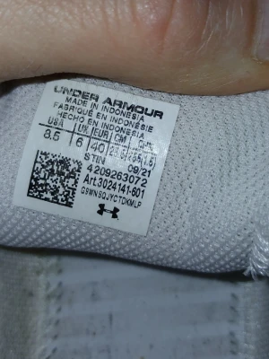 Under Armour vita och beige sneakers - Snygga sneakers från Under Armour i vitt och beige med en röd logga på sidan. Skorna har vita skosnören och en dämpad sula med Charge-teknologi. Ovandelen är i meshmaterial för bra andningsförmåga och komfort. Perfekta för en sportig och trendig look.