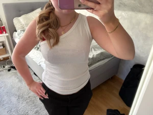Vit ribbad ärmlös linnetopp - Säljer en vit ribbad linnetopp med rund halsringning och ärmlös design. Toppen är figurnära och har en enkel, stilren look som passar perfekt till både jeans och kjol. Materialet känns mjukt och stretchigt för en bekväm passform.