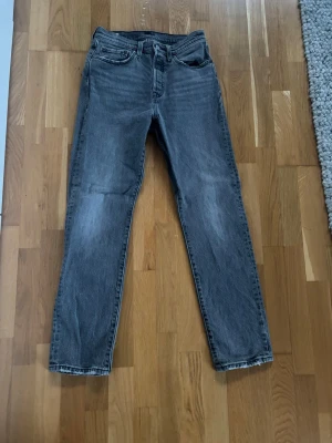 Grå raka jeans från Levi's - Snygga grå jeans från Levi's med rak passform och klassiska fem fickor. Jeansen har en vintage tvätt och tydliga sömmar, samt den ikoniska Levi's-lappen bak i midjan. Perfekta för en avslappnad och trendig look.
