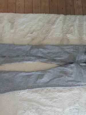 Grå bootcut lowrise jeans - Säljer ett par grå jeans i tvättad denim med raka ben och klassisk femficksmodell. Jeansen har normalhög midja och synliga sömmar i mörkare grått. Perfekta för en avslappnad och trendig look.