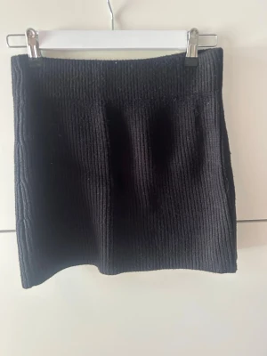 Svart ribbad kjol från Zara - Säljer en svart ribbad kortkjol från Zara. Kjolen är stickad och har en enkel, tight passform som sitter snyggt på kroppen. Perfekt att matcha med en oversized tröja eller crop top för en trendig look.