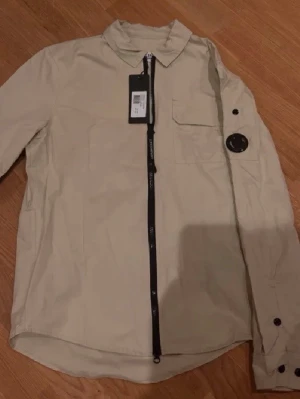 Beige overshirt från C.P. Company - Stilren beige overshirt från C.P. Company med svart dragkedja.