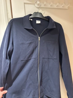 Mörkblå overshirt från Selected Homme | S - Overshirten är använd endast en enstaka gång. Snygg mörkblå overshirt från Selected Homme med två stora bröstfickor och hel dragkedja framtill. Overshirten har klassisk krage och är tillverkad i mjuk bomull, perfekt för lager-på-lager-stil.