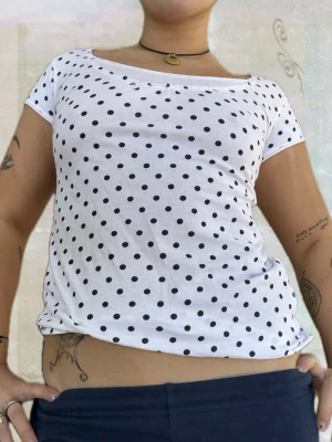 Vit prickig t-shirt med rund hals - Vit t-shirt med svarta prickar och rund halsringning. Modellen är kortärmad och har en avslappnad passform. Perfekt för en trendig och lekfull stil. Tillverkad i mjuk bomull som känns skön mot huden.