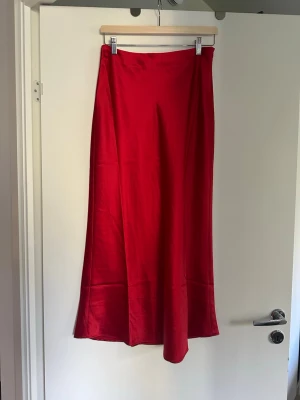 Röd midikjol i satin  - Snygg röd midi skirt från NA-KD i glansigt satinmaterial. Kjolen har en enkel och stilren design med lätt utställd passform som ger ett elegant fall. Perfekt för dig som vill sticka ut med färg och stil.
