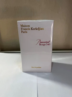 Baccarat Rouge 540 Eau de Parfum - Maison Francis Kurkdjian Baccarat Rouge 540 Eau de Parfum i elegant vit kartong med guld- och rödfärgad text. Lyxig och ikonisk doft som kommer i en rektangulär förpackning. Perfekt för dig som vill ha en exklusiv parfym med unik karaktär.