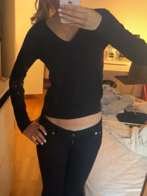 Svart långärmad topp med v-ringning - Snygg svart långärmad topp med v-ringning och figurnära passform. Perfekt att matcha med jeans eller kjol för en stilren look. Enkel och stilren design utan synliga detaljer eller mönster.