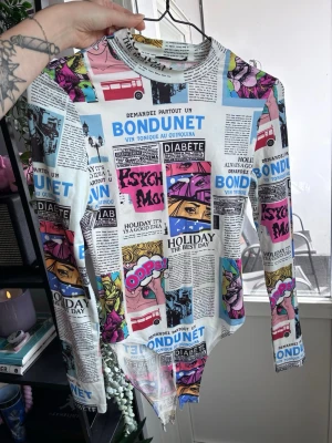Färgglad body med tidningsmönster - Unik body med lång ärm och coolt tidningsinspirerat tryck i flera färger som blått, rosa, gult och svart. Materialet är stretchigt och mjukt, perfekt för dig som vill sticka ut. Rund halsringning och tryckknappar i grenen för enkel på- och avtagning.