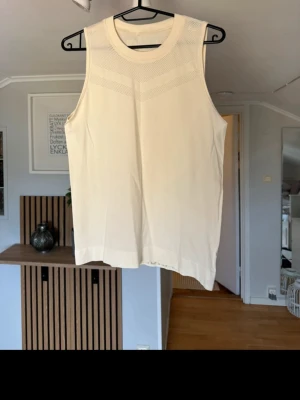 Beige ärmlös stickad linnetopp - Snygg beige ärmlös linnetopp med rund halsringning och diskret stickat mönster upptill. Toppen har en rak passform och är perfekt för varmare dagar. Materialet är stickat och känns mjukt mot huden.