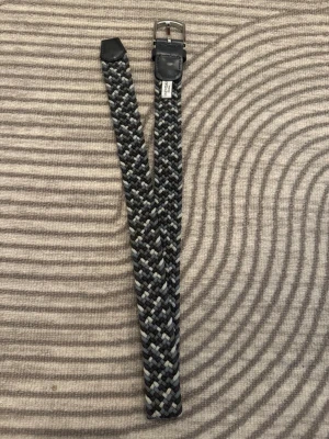 Blått/grått/vitt Flätat bälte från OneWear  - Snyggt flätat bälte från OneWear i olika nyanser av grått, svart och vitt. Bältet har detaljer i mörkblått skinn och ett klassiskt spänne i silverfärgad metall. Perfekt accessoar för att lyfta din outfit.