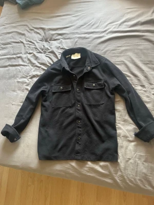Mörkblå overshirt från Selected - Stilren mörkblå overshirt från Selected med klassisk krage och knäppning framtill. Två bröstfickor med lock och knappar ger en snygg detalj. Tillverkad i ett kraftigare bomullstyg som passar perfekt som lager på lager-plagg. Funkar perfekt till höst/tidig sommar även under sommarkvällarna! Storlek L men funkar även som en M