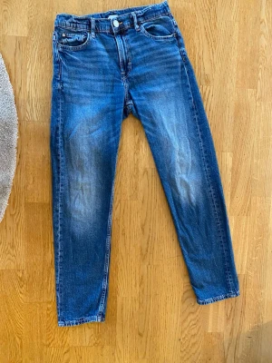 Blå raka jeans med slitningar - Snygga blå jeans med raka ben och lätt slitna detaljer framtill. Klassisk femficksmodell med knapp och dragkedja. Jeansen har en cool tvättad look och är tillverkade i denim. Perfekta för en avslappnad stil.