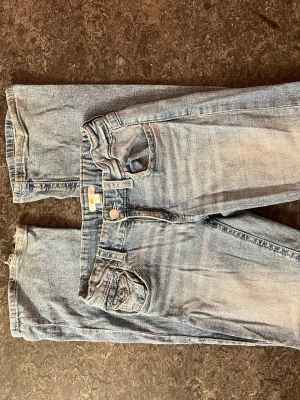 Ljusblå lowwaist jeans med knappar - Säljer ett par ljusblå jeans, lowwaist, knappar på fickorna, storlek 170 men passar 34,36,S ( lite slitna längst ner )