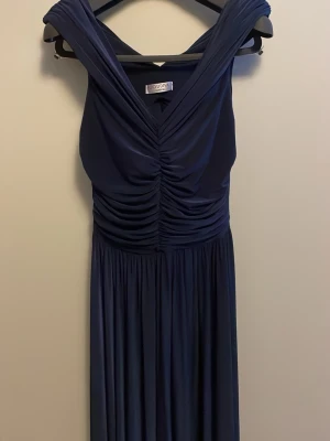 Marinblå långklänning från Goddiva - Supersnygg marinblå långklänning från Goddiva med offshoulder-design och v-ringad överdel. Klänningen har draperad byst, markerad midja och ett svepande, flowy kjolparti med slits. Perfekt för bal eller fest! OBS: Sälj i befintligt skick då den har använts, men endast en kväll på min bal i nian. Hör av dig vid intresse!😊