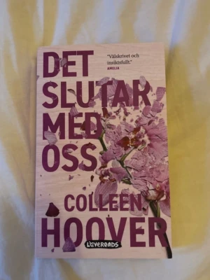 Det slutar med oss av Colleen Hoover - En svensk pocketbok av Colleen Hoover med titeln 'Det slutar med oss'. Omslaget är ljusrosa med lila text och blommotiv. Boken är utgiven av Lovereads och tillhör genren skönlitteratur. Perfekt för dig som gillar känslosamma och gripande berättelser.