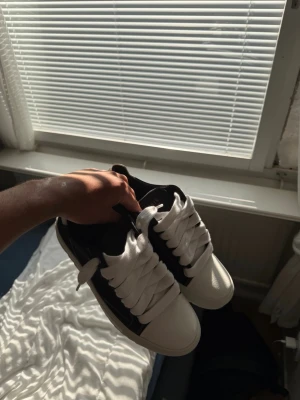Numeris skor storlek 45 - Snygga sneakers i svart och vitt med breda vita skosnören och en chunky vit sula. Skorna har låg profil och en stilren design som passar till det mesta. Materialet ser ut att vara en mix av läder och syntet. Perfekta för dig som gillar en clean och modern look.