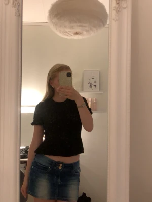 Svart stickad topp med volang - Säljer en svart stickad topp med korta ärmar och volangkant nedtill. Toppen har en rund halsringning och ribbstickade detaljer vid ärmslut och nederkant. Perfekt till jeans eller kjol för en trendig look.