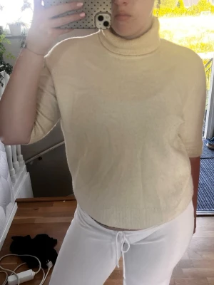 Beige stickad polotröja - Säljer en beige stickad polotröja med halvlånga ärmar och ribbade muddar. Tröjan har en hög polokrage och är i mjukt material, perfekt för lager på lager. Enkel och stilren design som passar till det mesta.