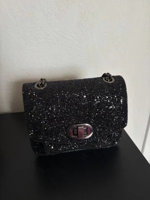 Svart glittrig axelremsväska - Snygg svart handväska täckt av glitter. Passar perfekt till fest eller för dig som vill sticka ut!