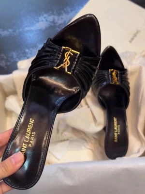 Svarta Saint Laurent pumps med gulddetalj - Snygga svarta pumps från Saint Laurent i glansigt läder med spetsig tå och öppen häl. Skorna har en elegant guldfärgad YSL-logga framtill och smal klack. Perfekta för dig som vill ha en lyxig och trendig look.