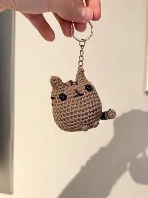 Handvirkad Pusheen nyckelring  - Söt handvirkad nyckelring i form av Pusheen-katten. Perfekt att hänga på väskan eller nyckelknippan för en gullig touch. Tillverkad i bomullsgarn metallkedja och fylld med polyestervadd.