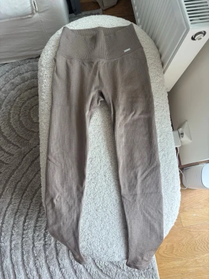 Ribbade beigea leggings med hög midja - Snygga ribbade leggings i en mjuk beige nyans med hög midja. De är stretchiga och har en figurnära passform som framhäver siluetten. Perfekta för en avslappnad och trendig look. Materialet ser ut att vara bomullsblandning eller liknande för extra komfort.