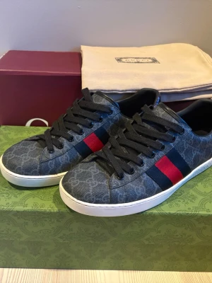 Gucci sneakers  - Snygga Gucci ace sneakers i mörk färg. Dessa Gucci ace sneakers är perfekta till skolstarten då dom är riktigt feta. Dojjorna  är användna varsamt och de är därför i väldigt bra skick. Det är bara att höra av dig om du har frågor. Två boxar, extra snören och Gucci påse tillkommer.