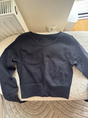 Svart ribbad långärmad tröja - Snygg svart långärmad tröja med ribbad struktur och bred mudd nedtill. Tröjan har rund halsringning och är tillverkad i ett mjukt, stretchigt material som sitter skönt på kroppen. Perfekt att matcha med jeans eller kjol.