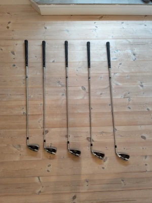 Järnset 6-Pw,Sw - Säljer ett set med fem golfklubbor från spalding. Klubborna har silverfärgade skaft i metall och svarta handtag. Klubbhuvudena är svarta och silver med röda detaljer och märkningen Dunlop. Perfekt för dig som vill börja spela golf eller behöver extra klubbor. 6-P, SW. Pw har en lite buckla på skaftet men inget som påverkar spelet