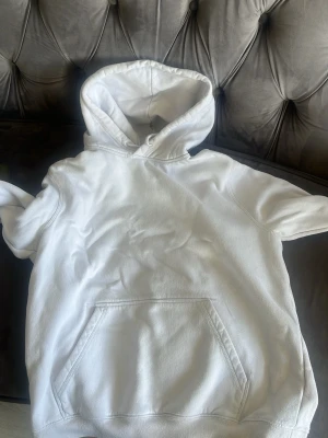 Vit hoodie med huva och magficka - Säljer en klassisk vit hoodie med stor huva och rymlig magficka. Hoodien har en avslappnad passform och är tillverkad i mjukt bomullstyg. Perfekt för en chill och enkel stil.