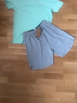 Ljusgrå träningsshorts från Nike - Snygga ljusgrå träningsshorts från Nike med elastisk midja och diskret logga på benet. Perfekta för gymmet eller löprundan. Lätta och luftiga med klassisk passform.