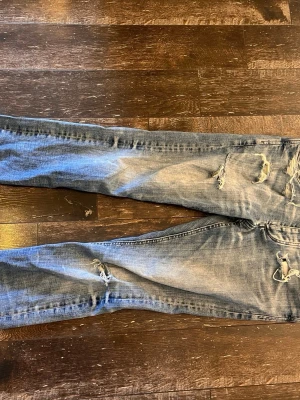 Ljusblå slitna jeans med hål - Säljer ett par ljusblå jeans med trendiga slitningar och hål på benen. Jeansen är slim fit i passform och klassisk femficksdesign. Perfekta för dig som gillar mer grisch stilen. Jeansen är ganska slitna men det går och fixa enkelt. 