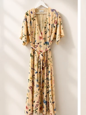 Blommig omlottklänning med knytband - Ljusbeige långklänning med blommigt mönster i rosa, blått och grönt. Klänningen har omlottmodell, v-ringning, korta ärmar och ett matchande knytband i midjan. Perfekt för sommarens alla tillfällen Använd en gång. Nypris 1499 kr.