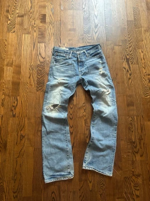 Ljusblå slitna jeans med raka ben - Ljusblå jeans med raka ben och slitningar på både fram- och baksida. Klassisk femficksmodell med detaljerade slitningar vid knän och lår. Jeansen har en avslappnad passform och är perfekta för en casual stil.