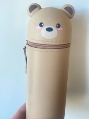 Pennfodral med björnmotiv - Sött beige pennfodral i form av ett björnhuvud med öron och ansikte, rosa kinder och dragkedja. Perfekt för att förvara pennor eller småsaker. 