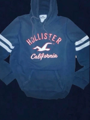 Hollister hoodie - Blå Hollister hoodie i prima skick inga defekter endast en lös tråd/hål! Skriv till mig om du undra nått eller vill ha mått är alltid aktiv! Bilden är tyvärr lite dålig som gör det att se ut som fläckar på den