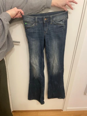 Blå bootcut jeans från Cheap Monday - Säljer ett par klassiska blå bootcut jeans från Cheap Monday, låg midja och gröna detaljer. Perfekta för en avslappnad och trendig look. Säljer då dom tyvärr var förstora,endast använda en gång.
