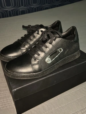 Svart Versus Versace skokartong - Säljer en svart skokartong från Versus Versace med tydlig logga på locket och en svart tygpåse inuti. Perfekt för dig som vill ha originalförpackning till dina Versace-skor eller för förvaring av accessoarer. Storlek 39 men passar pven 40,5